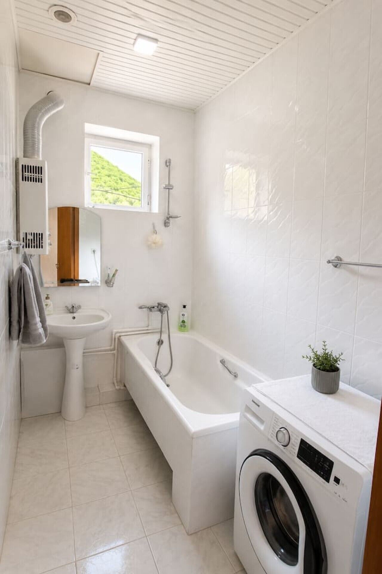 A compact bathroom with a sink, bathtub, and washing machine.