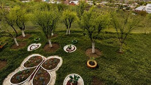 A landscaped garden with trees, a winding path, and a view of a town with buildings and mountains in the background. - Spacious Forest Guesthouse in Vanadzor for Families & Groups (Vanadzor)