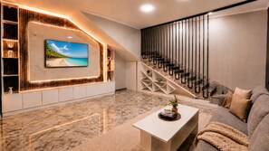 Sala de estar moderna com uma televisão grande, uma escada e piso de mármore.