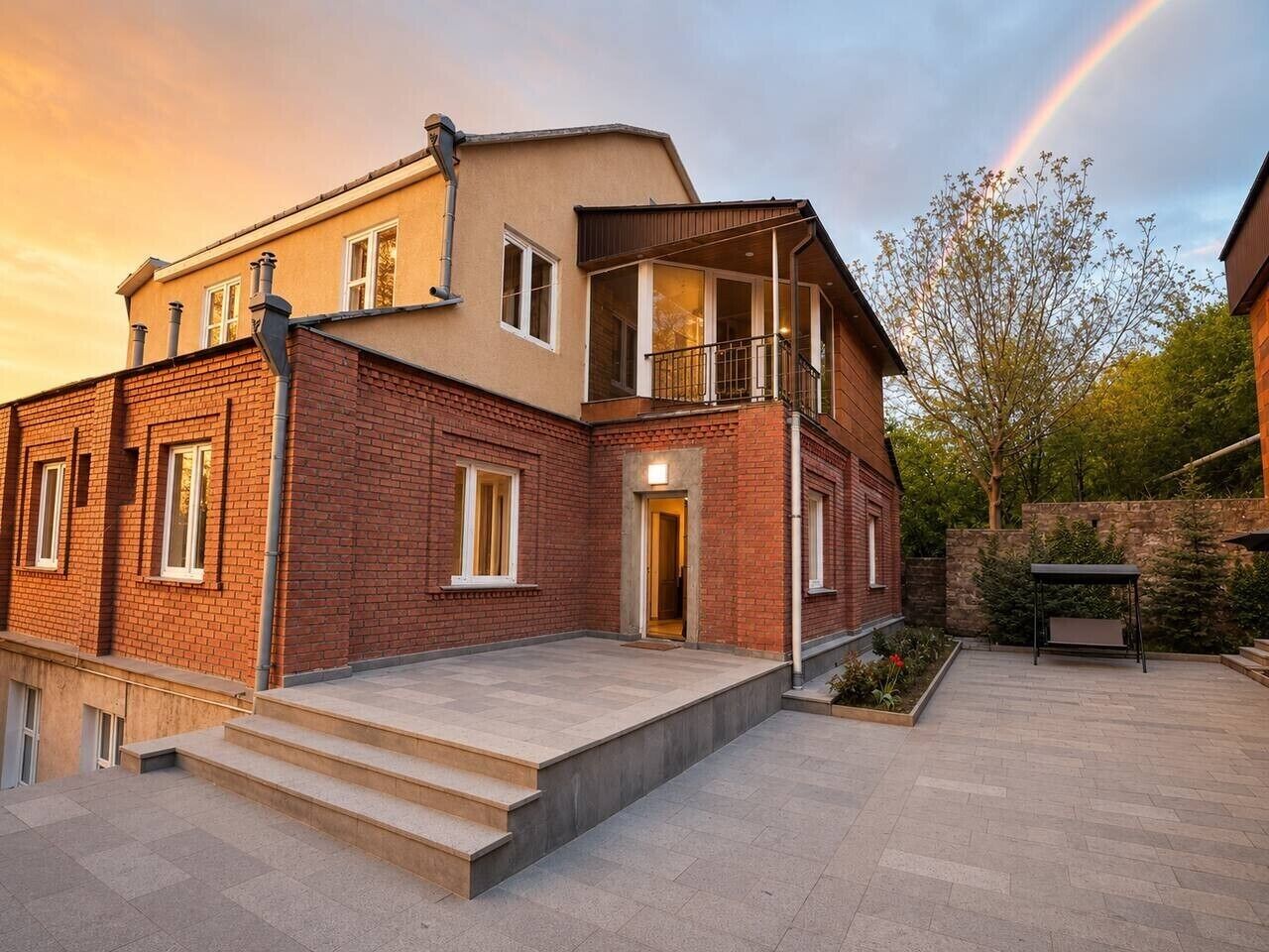 Une maison à deux étages dotée d’un balcon, d’une terrasse pavée et d’un mur en pierre.