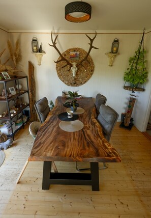 A dining area with a large wooden table, chairs, a wall-mounted deer skull decoration, and a hanging plant. - A Swedish-style house with horses and a canoe trail right outside the door (Värmland County)