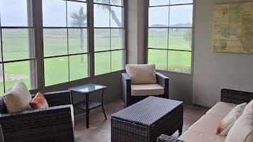 Une pièce spacieuse avec de grandes fenêtres, des meubles en osier, une petite table et une carte accrochée au mur.