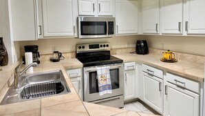 A kitchen with white cabinets, a stainless steel stove, a microwave, and a coffee maker. - Peaceful Beachwalk Escape! Updated 3rd-Floor Condo w/ Lanai, Pool & Hot Tub (Fort Myers)