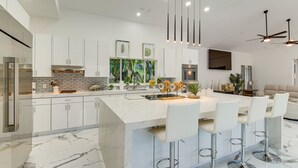 A modern kitchen with white cabinetry, a marble island, and bar stools.