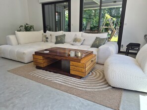 A modern living room with a sectional sofa, a wooden coffee table, and a large sliding glass door leading to a garden. - Villa with pool and spa in Anglet for 8-10 people (Anglet)