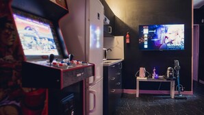 A room with a gaming console, a television, a small table with a coffee maker, and a vacuum cleaner. - 2-room apartment with air field hockey arcade machine and computer (Vitry-sur-Seine)