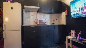 A kitchen with dark cabinets, a white refrigerator, a microwave, and a small table with a kettle and flowers. - 2-room apartment with air field hockey arcade machine and computer (Vitry-sur-Seine)