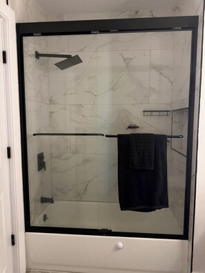 Eine begehbare Dusche mit Glaswand, schwarzem Rahmen, Marmorfliesen, einem Handtuchhalter und einer weißen Tür.