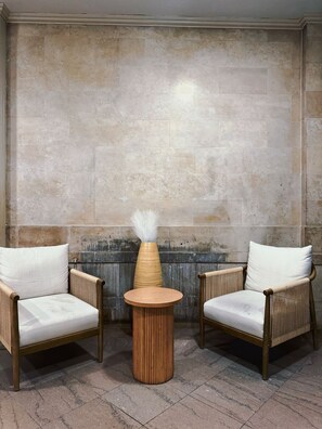 A room with two wicker chairs, a round wooden table, and a vase with white feathers.