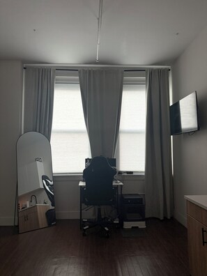 Ein Zimmer mit Schreibtisch, Stuhl und einem an der Wand befestigten Fernseher.