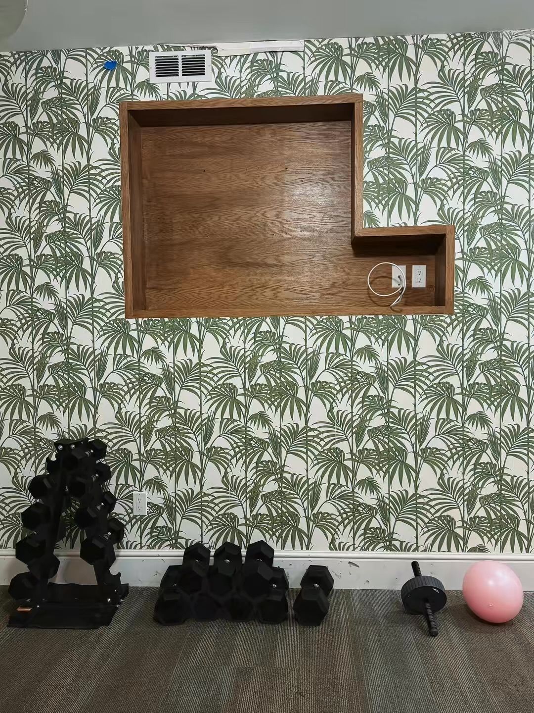 A room with a wooden shelf unit mounted on a wall with a tropical leaf pattern wallpaper.
