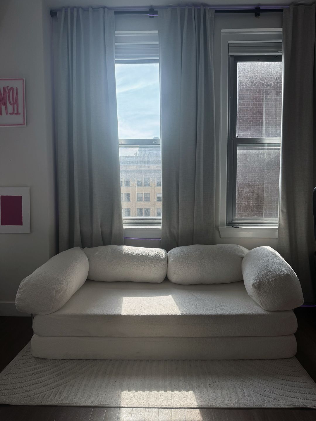 Una habitación con un sofá blanco, dos ventanas con cortinas, un cuadro en la pared y un tapete estampado.