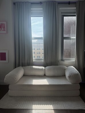 A room with a white sofa, two windows with curtains, a framed picture on the wall, and a patterned rug.