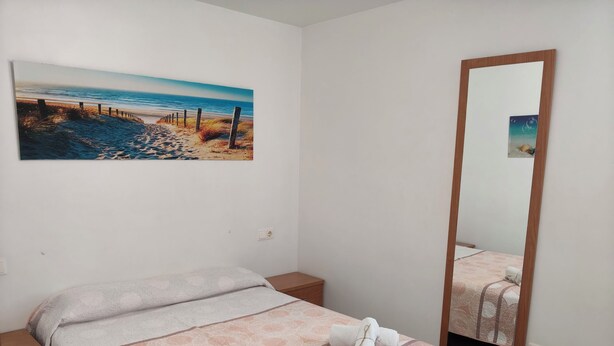A hotel room with a bed, a nightstand, a painting of a beach, and a mirror.