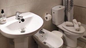 A bathroom with a sink, toilet, bidet, and shower curtain.
