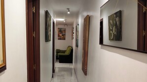 A hallway with a wooden bench, a green chair, and a wall-mounted TV.