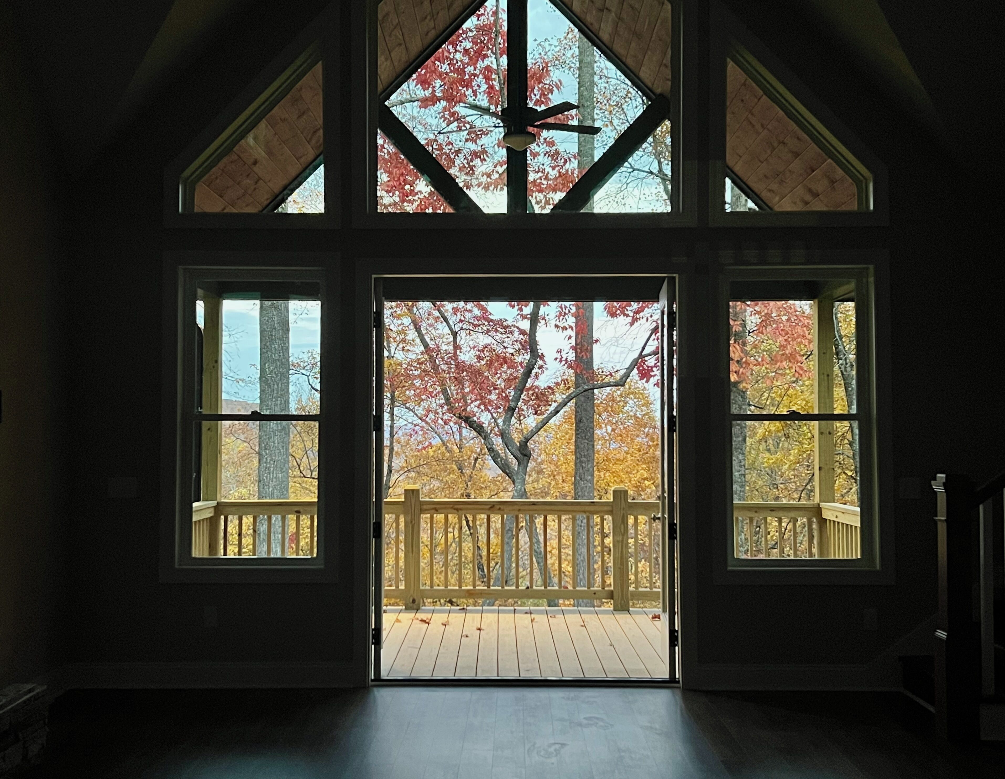 A room with a large open door leading to a wooden deck with a view of autumn trees.