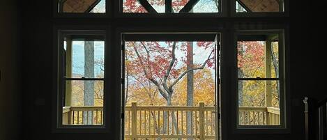 A room with a large open door leading to a wooden deck with a view of autumn trees.