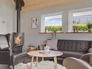 Ein gemütliches Wohnzimmer mit Kamin, einem grauen Sofa, einem runden Couchtisch und Blick ins Grüne.