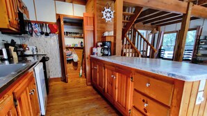 A wooden kitchen with a central island, wooden cabinets, and a visible staircase leading to another level.