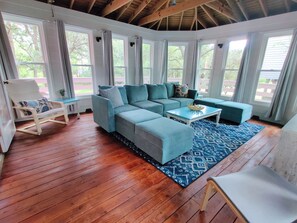 A room with a wooden floor, a sectional sofa, a small table, and a chair. - Private, Ocean Side, Walking Distance to Beach (Corolla)