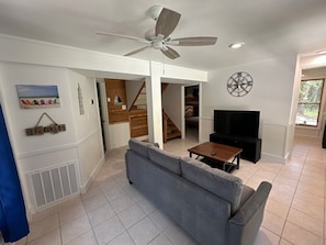 A living room with a grey sofa, a wooden coffee table, a TV, a ceiling fan, and a staircase leading to another room.