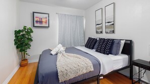 Een slaapkamer met een bed, een nachtkastje, een plafondventilator, een kamerplant en twee aan de muur hangende afbeeldingen.