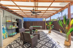 Ein überdachter Patio-Bereich mit Korbmöbeln, einem Deckenventilator und einem Billardtisch.