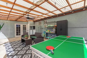 Ein überdachter Außenbereich mit einer Tischtennisplatte, Korbmöbeln und einem Deckenventilator.