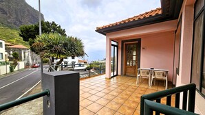 A balcony with a tiled floor, a table, chairs, and a door leading to an interior space. - Domus Dino (Porto da Cruz)