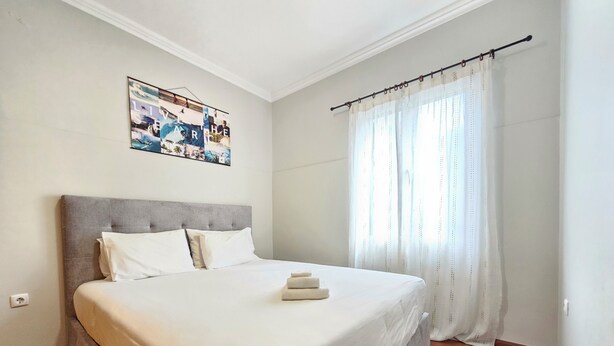 A neatly made bed in a room with a headboard, a wall-mounted artwork, and a window with curtains. - Domus Dino (Porto da Cruz)