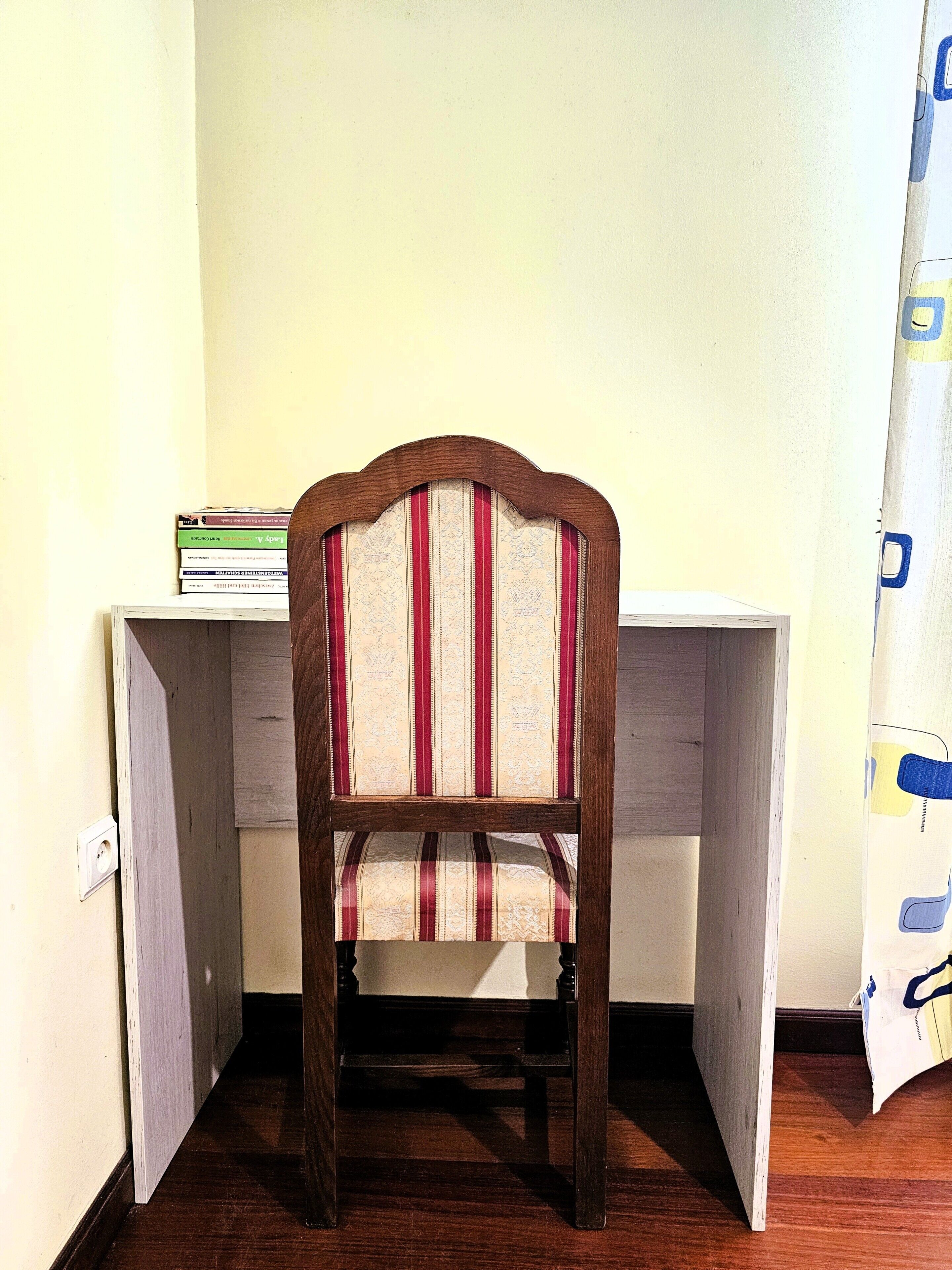 A corner desk with a chair, a stack of books, and a curtain.
