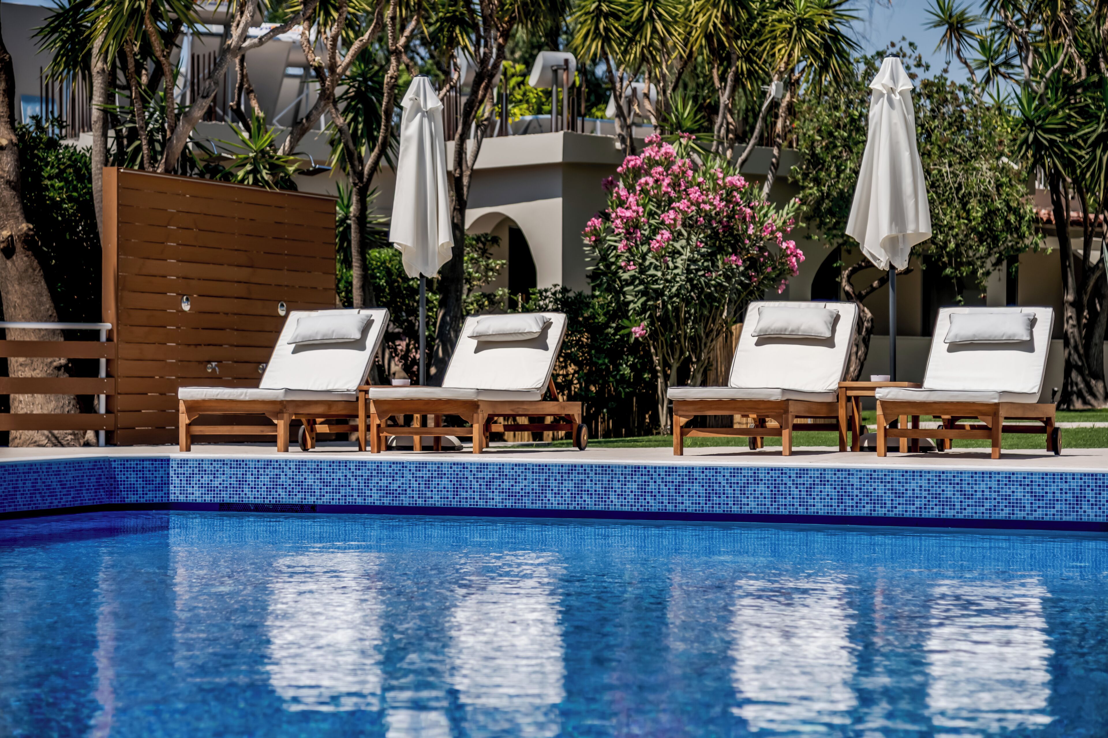 Une piscine entourée de verdure et d’un bâtiment, avec des chaises longues et des parasols.