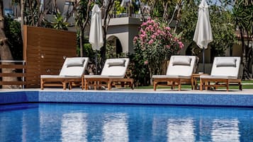 Une piscine entourée de verdure et d’un bâtiment, avec des chaises longues et des parasols.