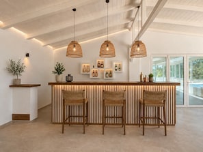 A modern kitchen with a wooden bar, three wicker pendant lights, and a potted plant on the counter.