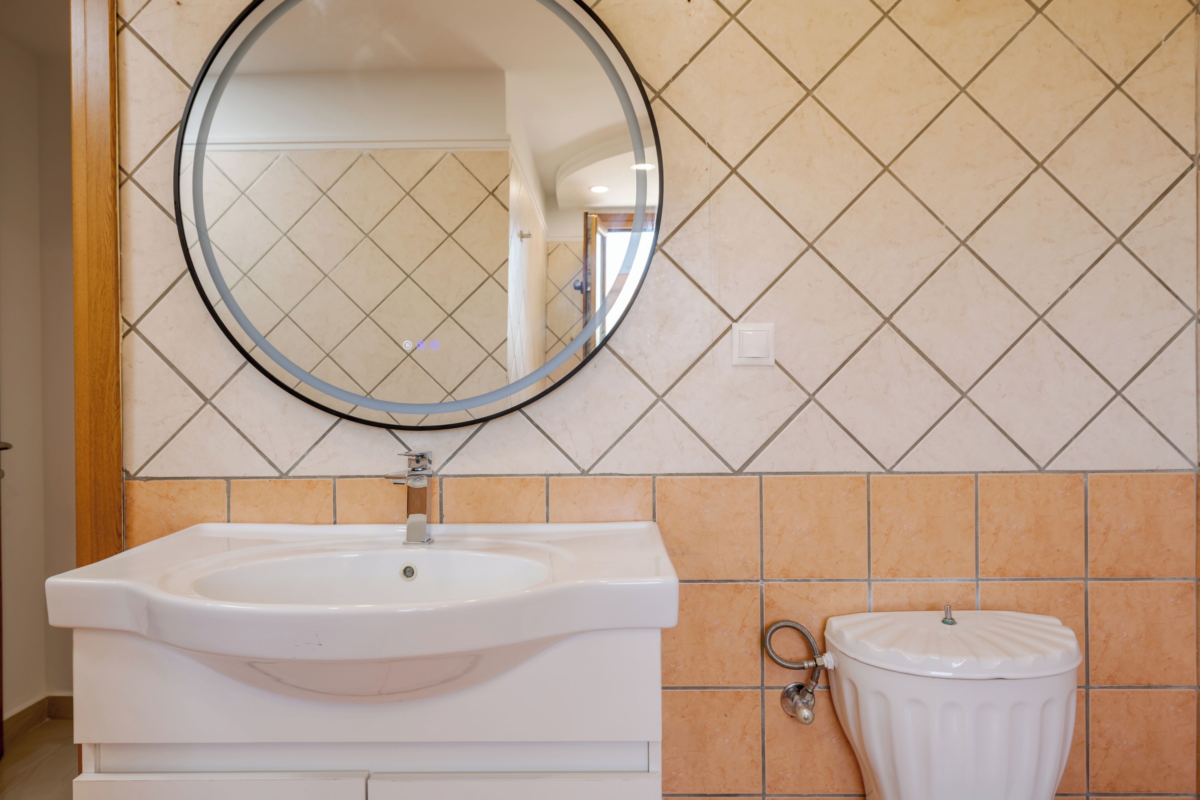 A bathroom with a white sink, a round mirror, and a toilet.