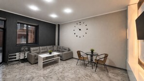 Uma sala de estar moderna com um sofá cinzento, uma mesa de centro branca e uma mesa redonda com cadeiras.