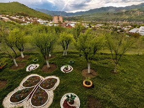 Un jardin aménagé avec des arbres et des jardinières, une vue lointaine d’une ville et des montagnes en arrière-plan.