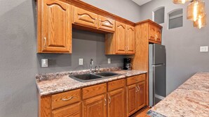 A kitchen with wooden cabinets, a granite countertop, a stainless steel refrigerator, and a coffee maker. - Riviera Paradise Lake Luxury (Sunrise Beach)