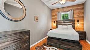 A bedroom with a wooden headboard, a round mirror, a bed with white bedding, two bedside lamps, and a small rug. - Riviera Paradise Lake Luxury (Sunrise Beach)