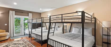 A hotel room with bunk beds, a sofa, a patterned rug, and a view of greenery outside.