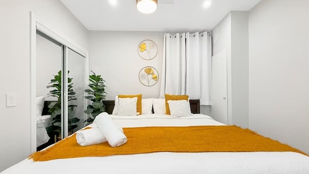 Een hotelkamer met een groot bed, een spiegel, een kamerplant en een muur met twee ronde decoratieve objecten.