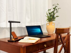 Un escritorio de madera con una computadora portátil, un libro, un bolígrafo, una lámpara y un florero con una planta.