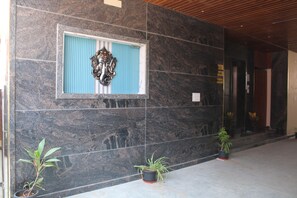 Um hall com paredes de mármore escuro, uma obra de arte emoldurada e plantas em vasos.