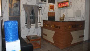 A reception desk with 'JP RESIDENCY' engraved, a framed Buddha statue, a window with curtains, and a small wooden table. - JP Residency (Tiruvannamalai)