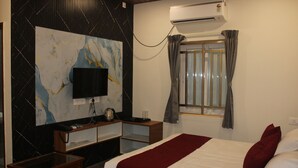 A hotel room with a bed, a TV, a desk, a coffee maker, and an air conditioning unit. - JP Residency (Tiruvannamalai)