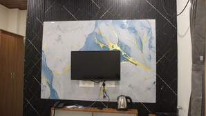 A modern bathroom with a large mirror, a black countertop with a coffee maker, and a mounted flat-screen TV. - JP Residency (Tiruvannamalai)