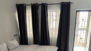 Quarto com cama, cortinas e vista pela janela.