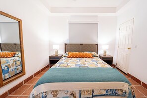 A bedroom with a bed, two bedside tables, a mirror, and a door.