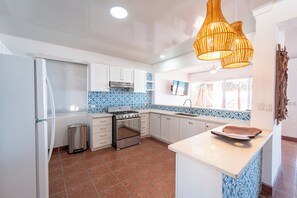 A kitchen with white cabinets, a stove, and a trash bin.